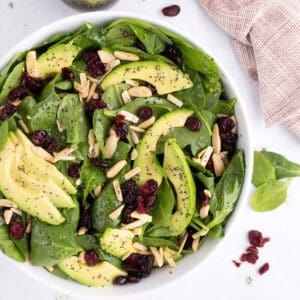 Bowl of spinach salad with avocados and almonds topped with dressing