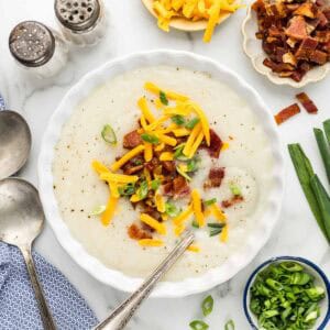 Potato soup in a bowl with a spoon surrounded by small dishes containing toppings.