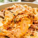 A serving of lasagna on a spoon over a large skillet with cheese stringing down.