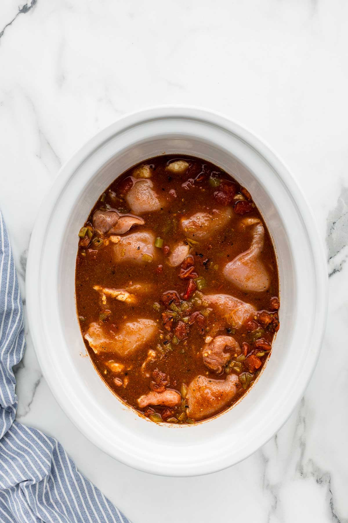 Crockpot with chicken thighs cooking in seasoned juices.