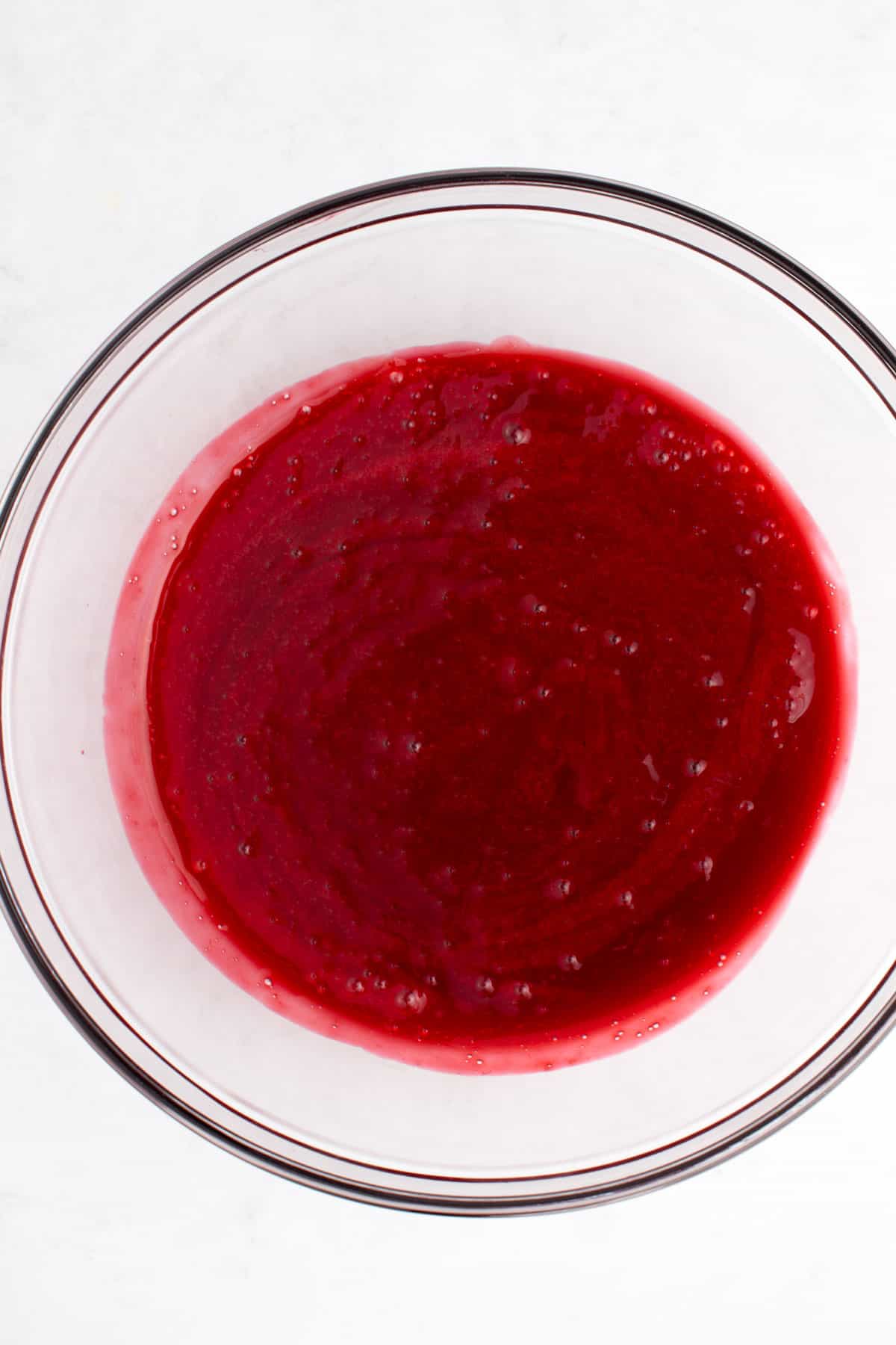 A glass mixing bowl of raspberry sauce.