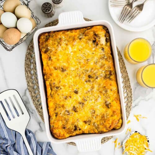 A breakfast biscuit casserole with an array of ingredients and utensils around it.