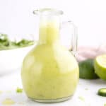 A tall bottle of jalapeno lime vinaigrette with a sprinkle of lime zest around it.
