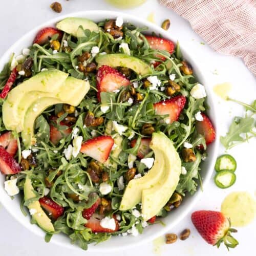 A large serving of strawberry arugula salad topped with lime jalapeno dressing.
