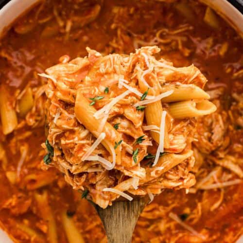 Shredded chicken pasta on a wooden spoon with a cooking pot behind it.