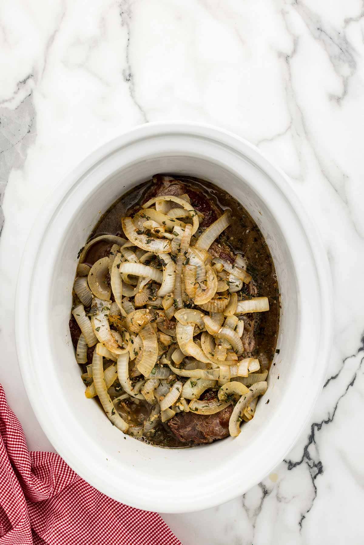 Onions added to a white crock pot of apple chuck roast.
