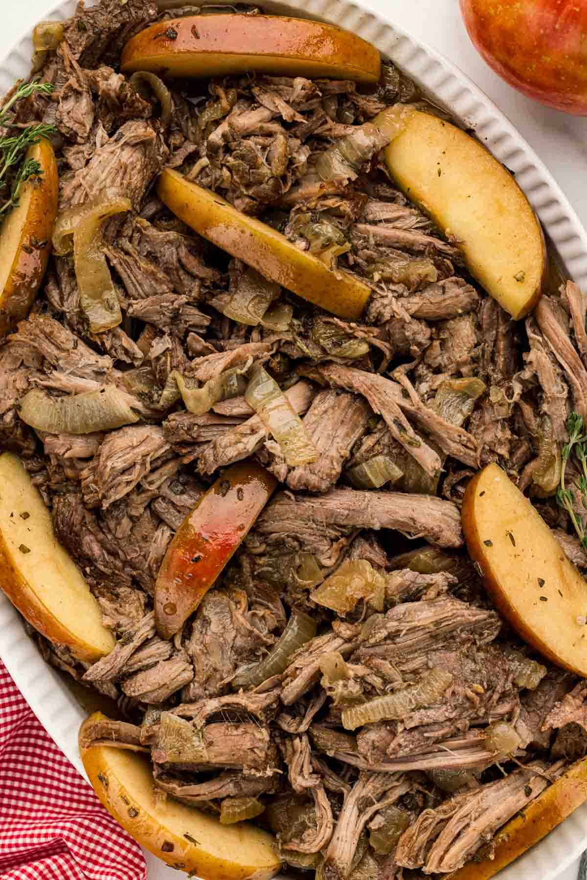 Chuck roast in a slow cooker with cooked apple slices.