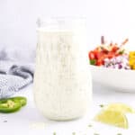 A glass jar full of Mexican dressing surrounded by salad ingredients.