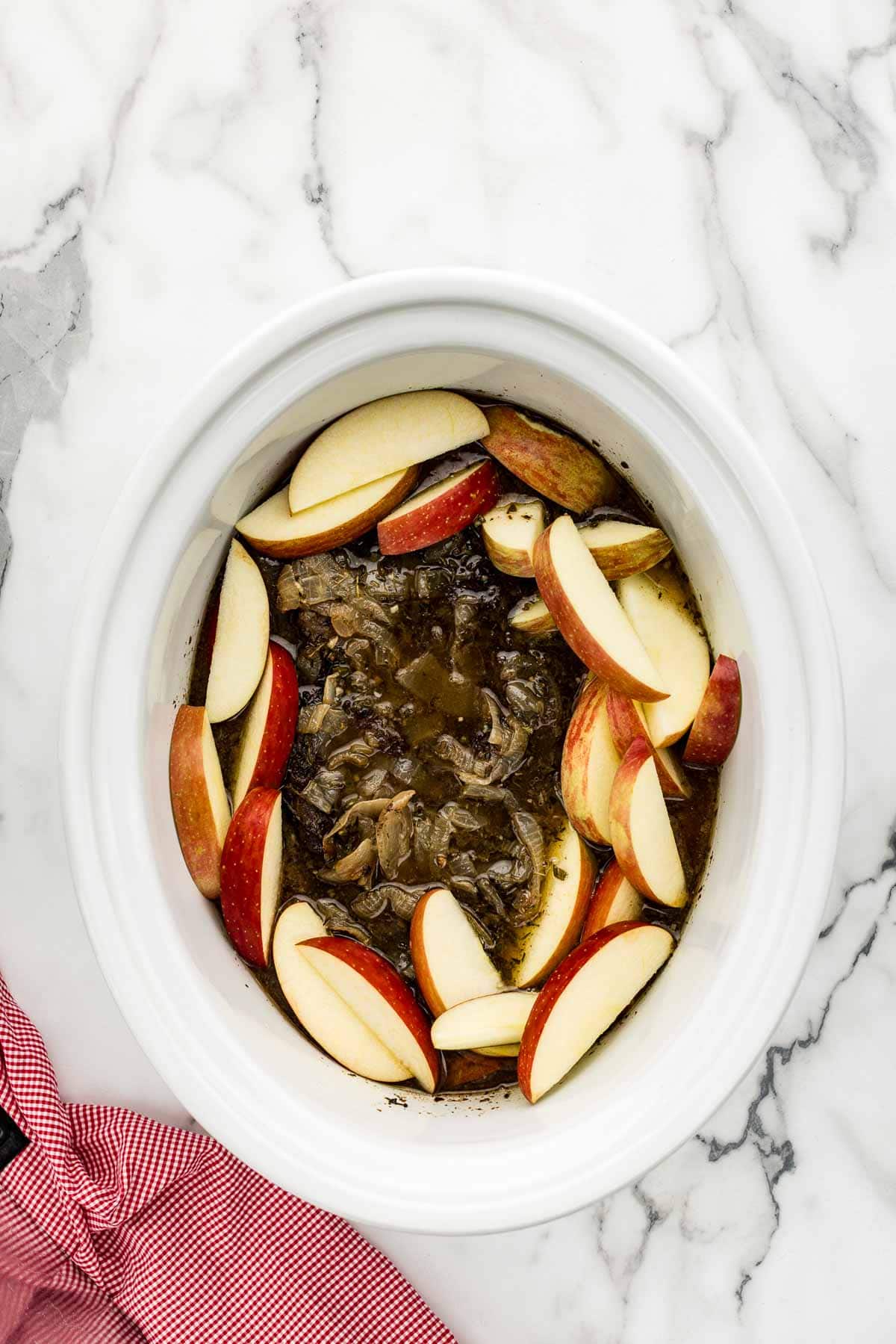 Raw apples added to a chuck roast in a slow cooker.