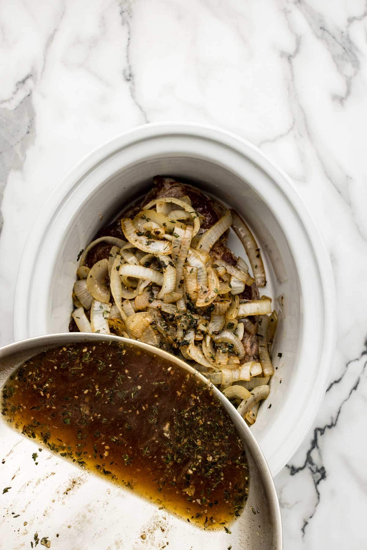 A skillet of juices getting poured into a slow cooker.