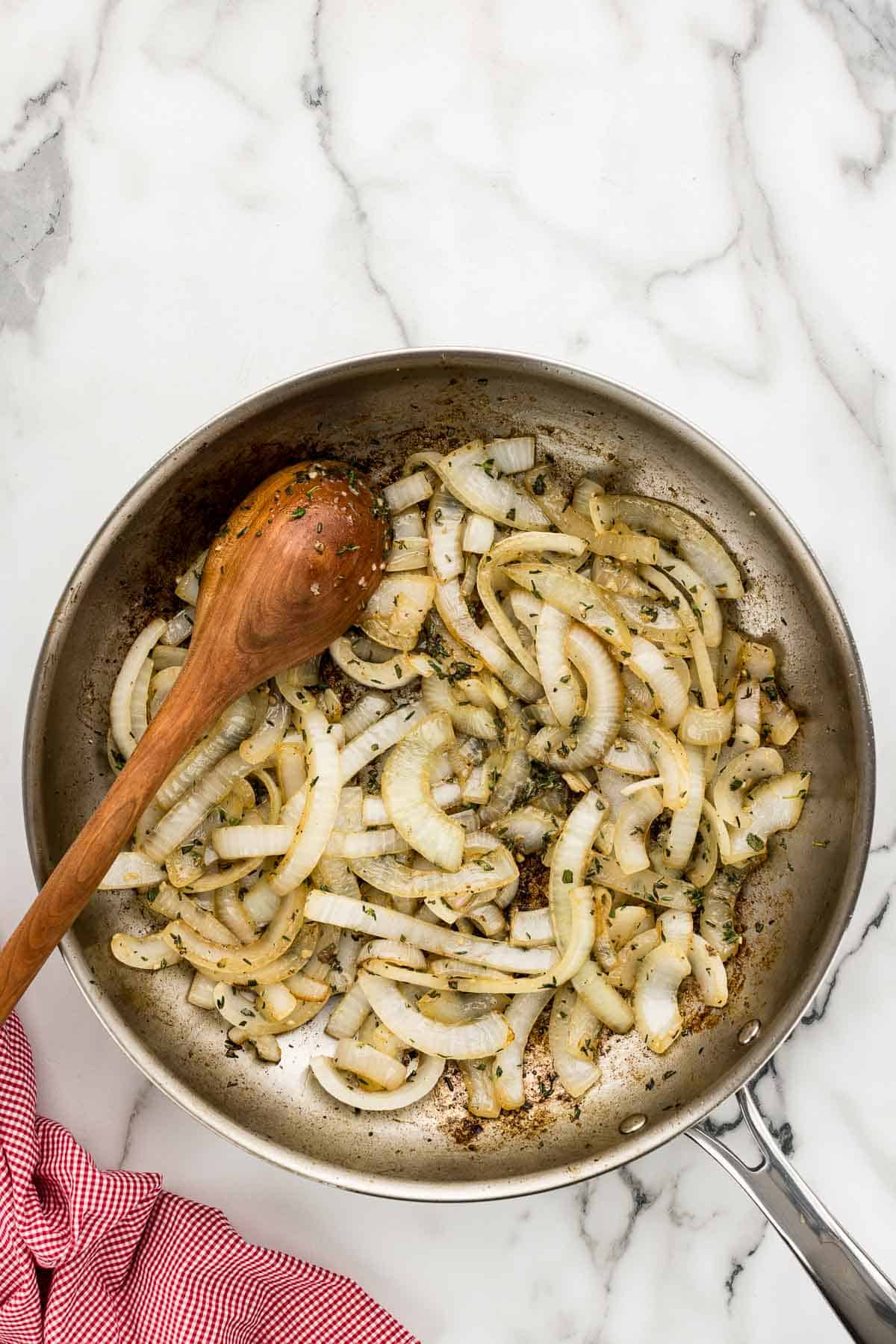 A pan of cooked onions with a wooden spoon.