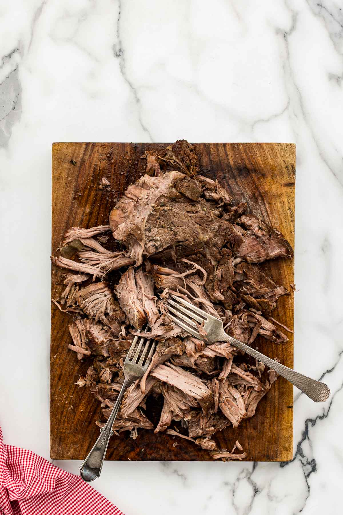Shredded beef on a cutting board with two forks.