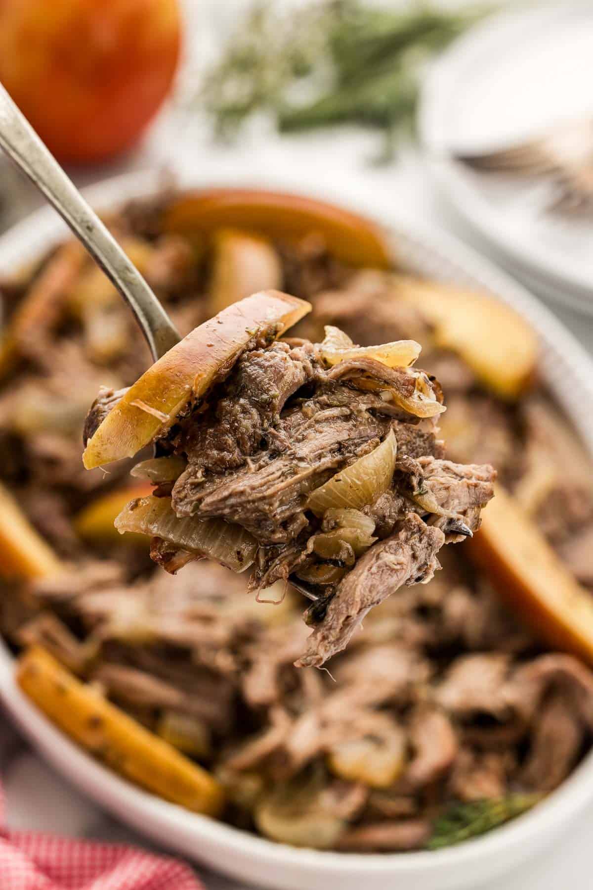 A spoonful of a pot roast with apples over a crock pot.