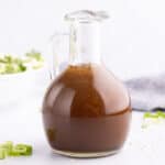 A tall glass pitcher half filled with simple Asian salad dressing.