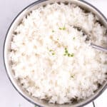 A cooking dish of moist jasmine rice with a spoon.