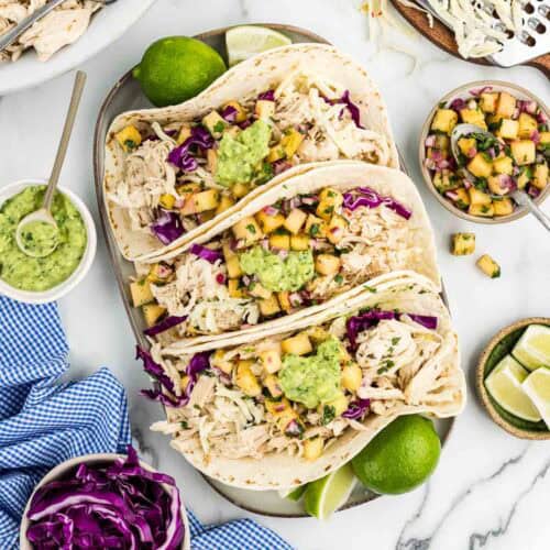 Three pineapple chicken tacos on a serving dish with limes.