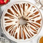 A whole bundt cake on a serving dish topped with icing and spices.