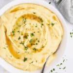 Mashed potatoes topped with herbs in a bowl with a spoon.