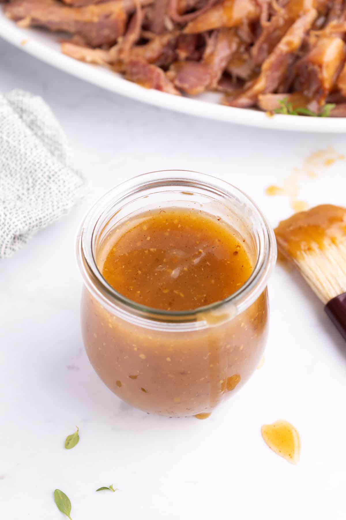 A jar of rum ham glaze with a sauce brush sitting beside it.