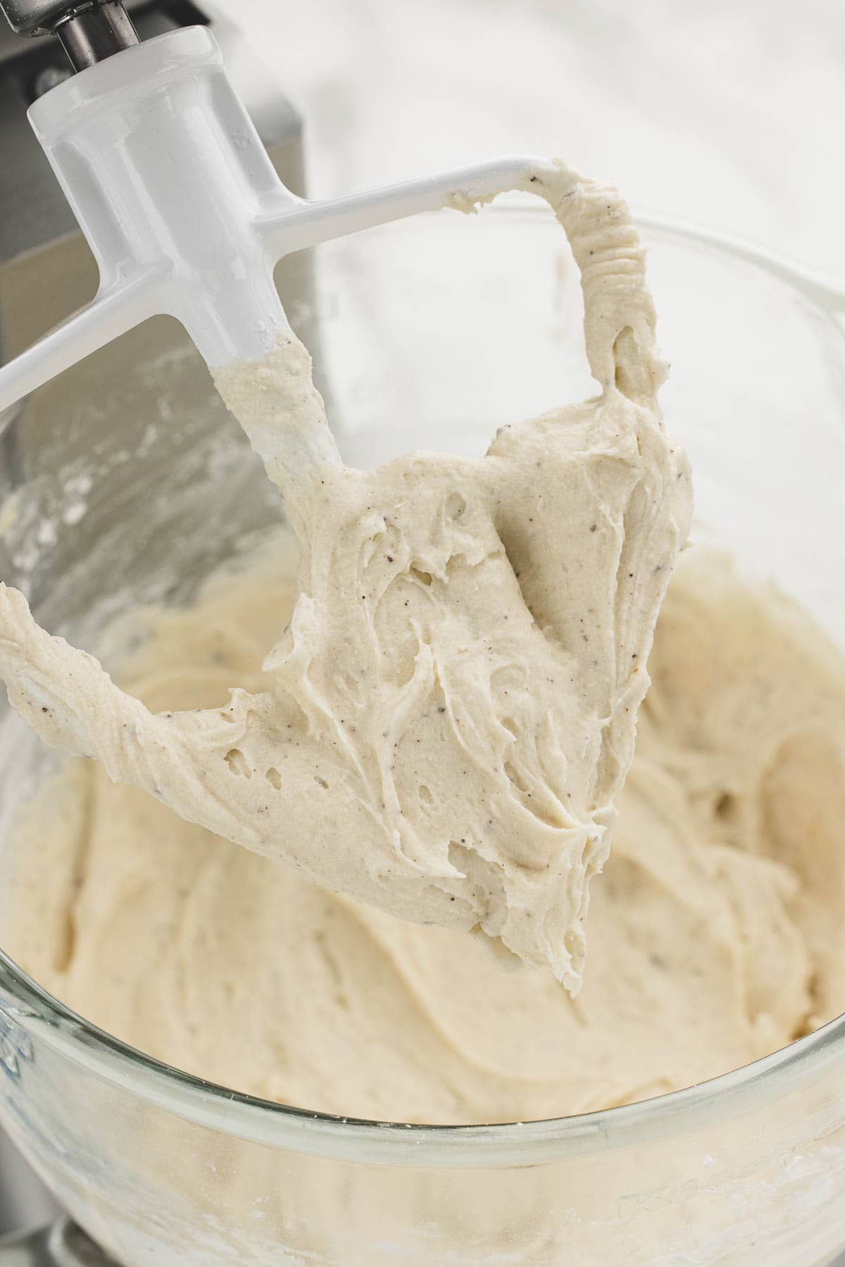 Closeup of a glass mixing bowl full of brown butter frosting under a stand mixer.
