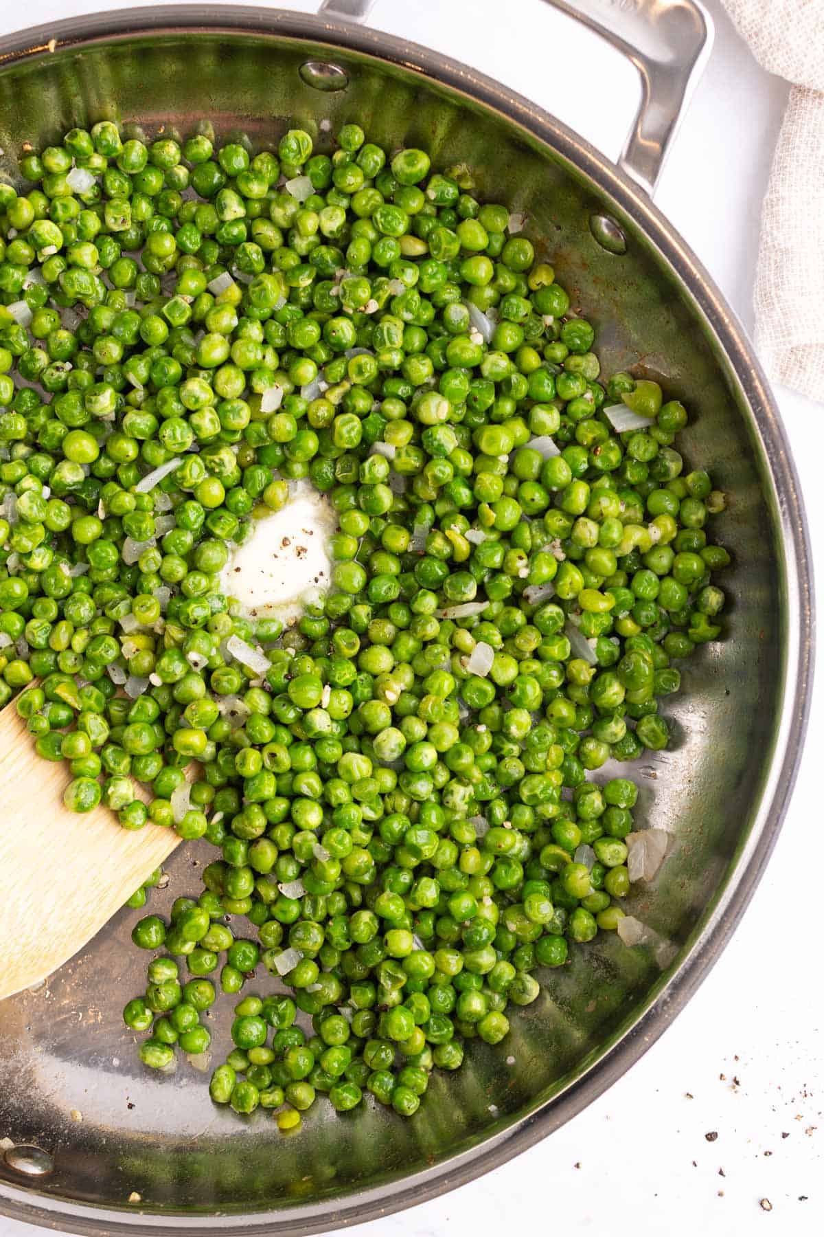 Buttery peas in a skillet with a wooden cooking tool.
