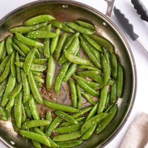 Sugar snap peas in a skillet with tongs beside it.