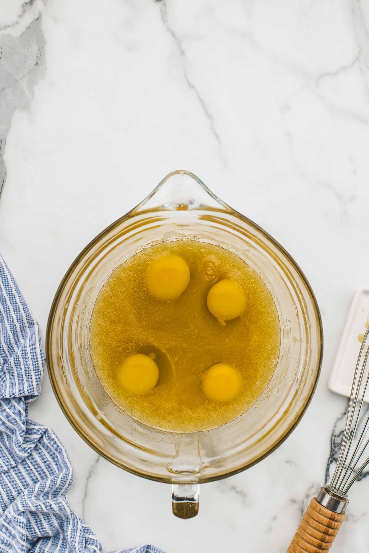 Eggs in a large mixing dish with a whisk beside it.