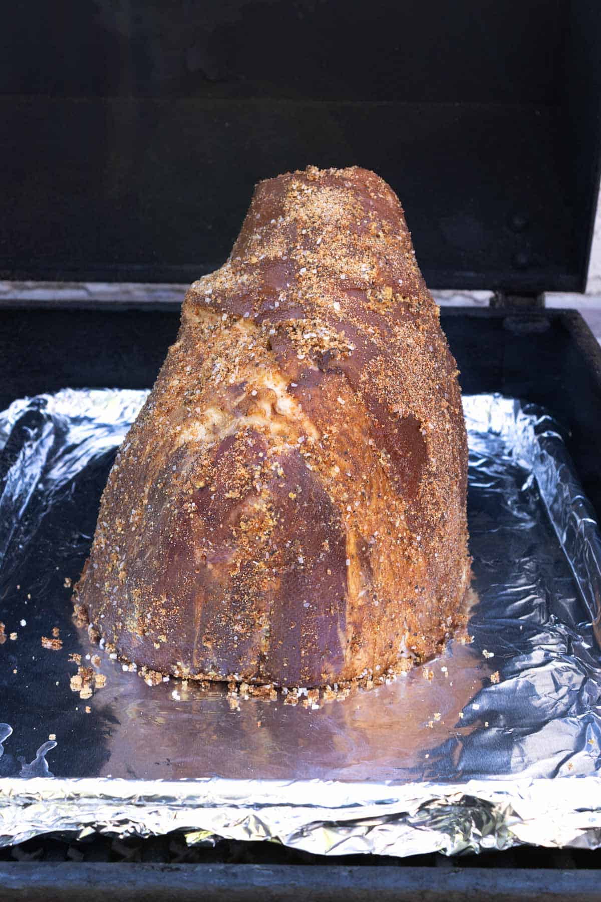 A seasoned ham on a tray in a smoker.