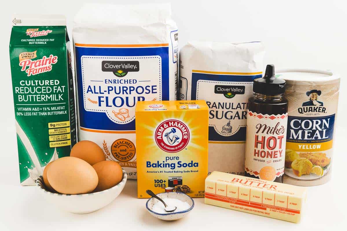 Eggs, salt, buttermilk, flour, baking soda, sugar, butter, hot honey, and corn meal on a countertop.