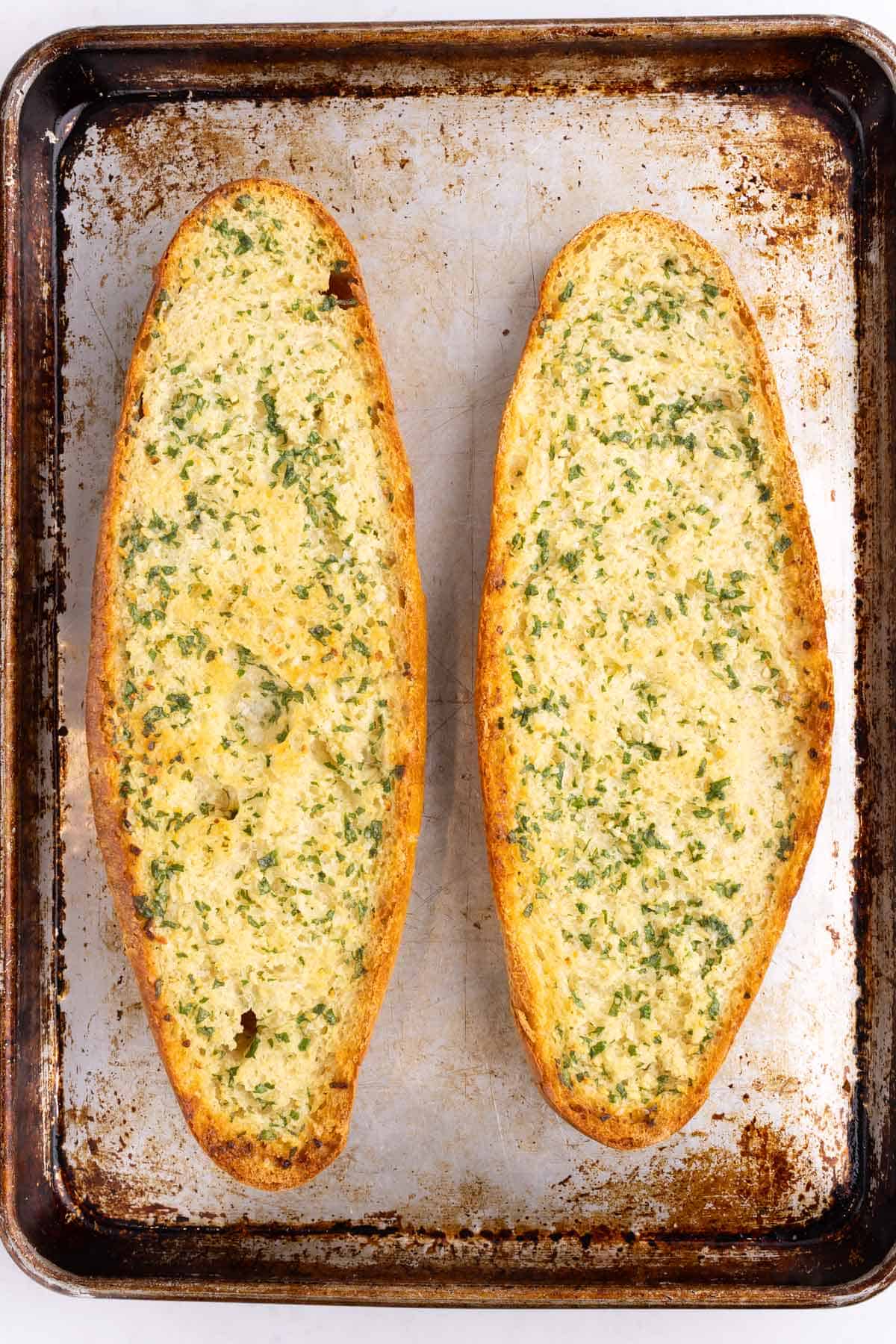 Two halves of baked garlic bread laid out on a sheet pan.