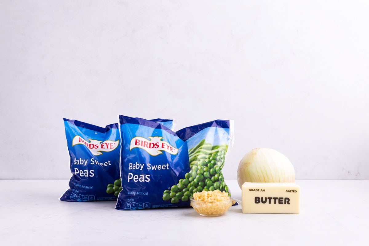 Frozen peas, garlic, an onion, and butter on a white countertop.