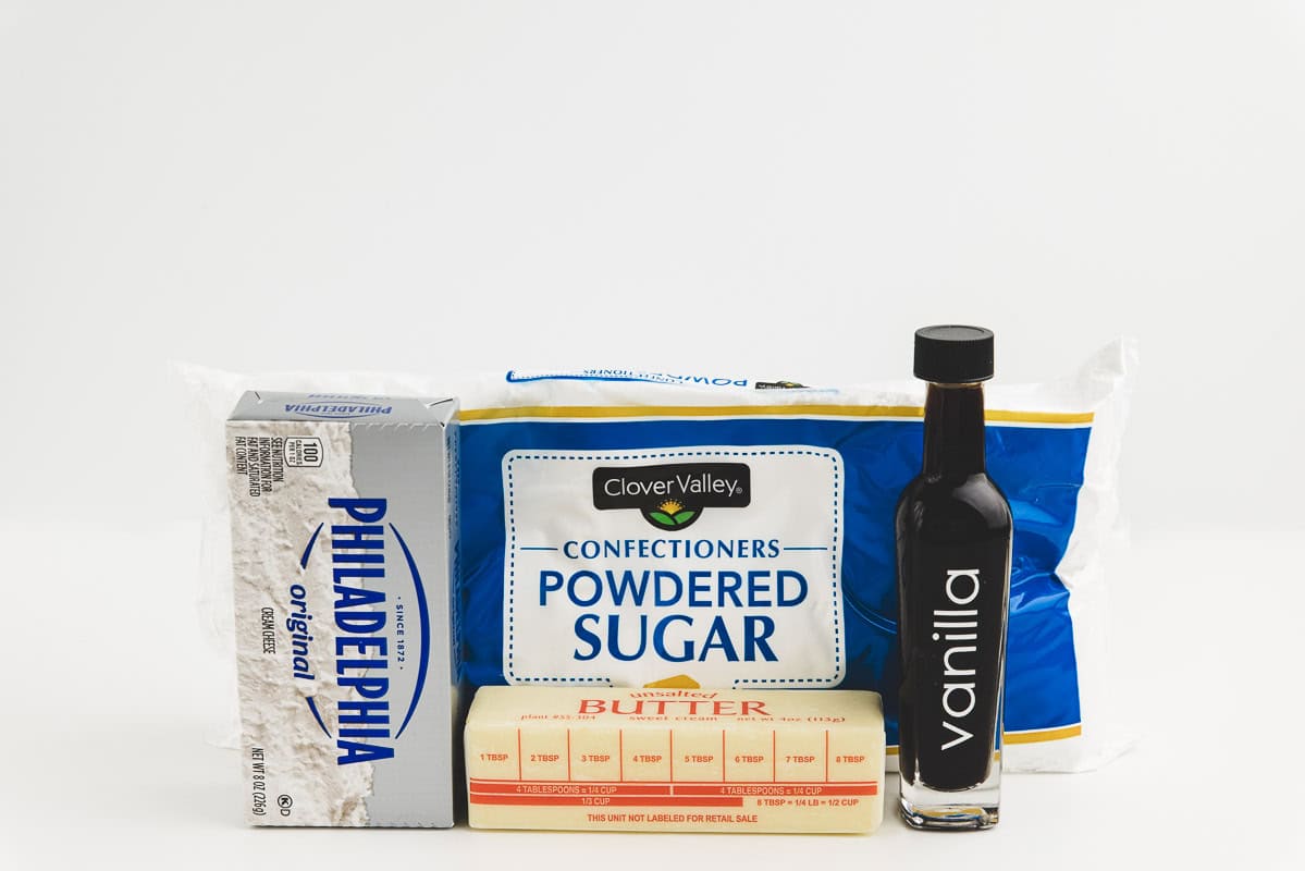 Butter, sugar, cream cheese, and vanilla on a white countertop.