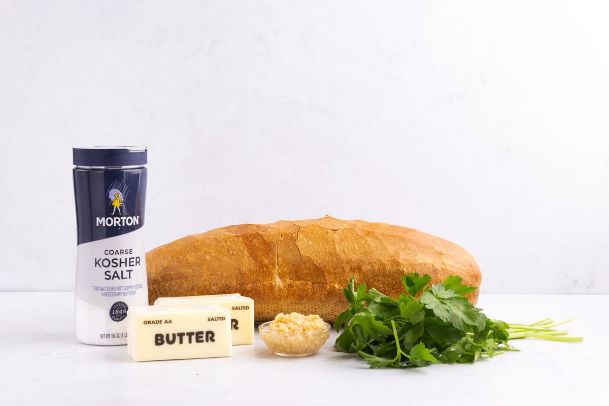 Butter, salt, garlic, herbs, and french bread on a counter.