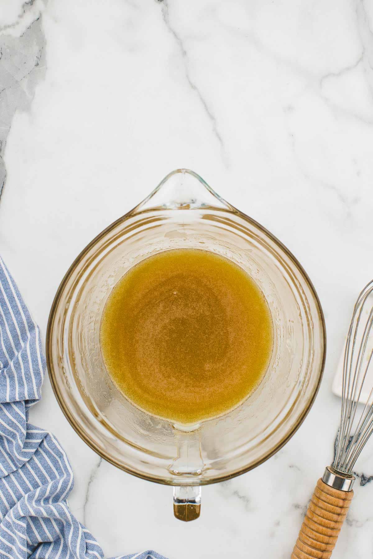 A glass dish of hot honey mixed together with a whisk.