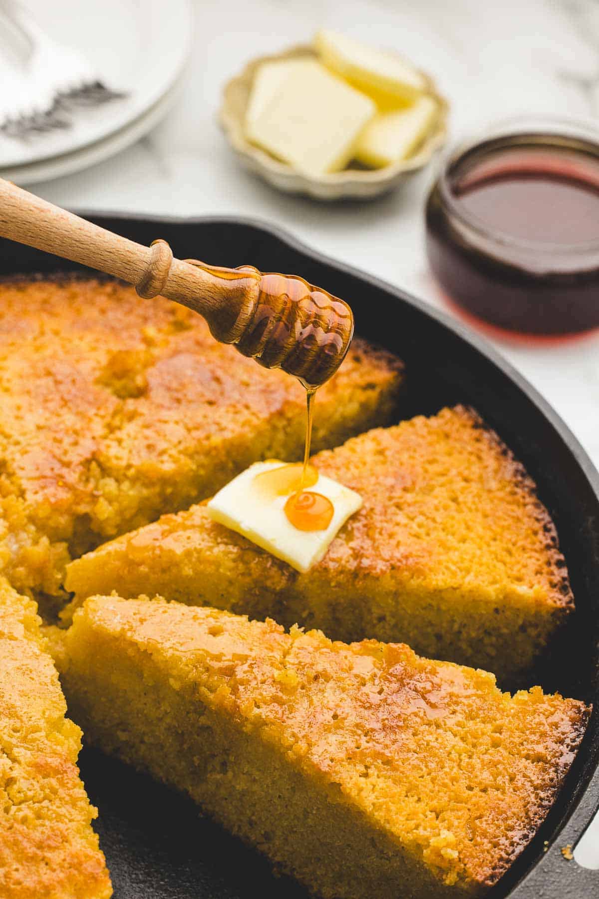 Hot honey drizzled over slices of cornbread in a cast iron pan.