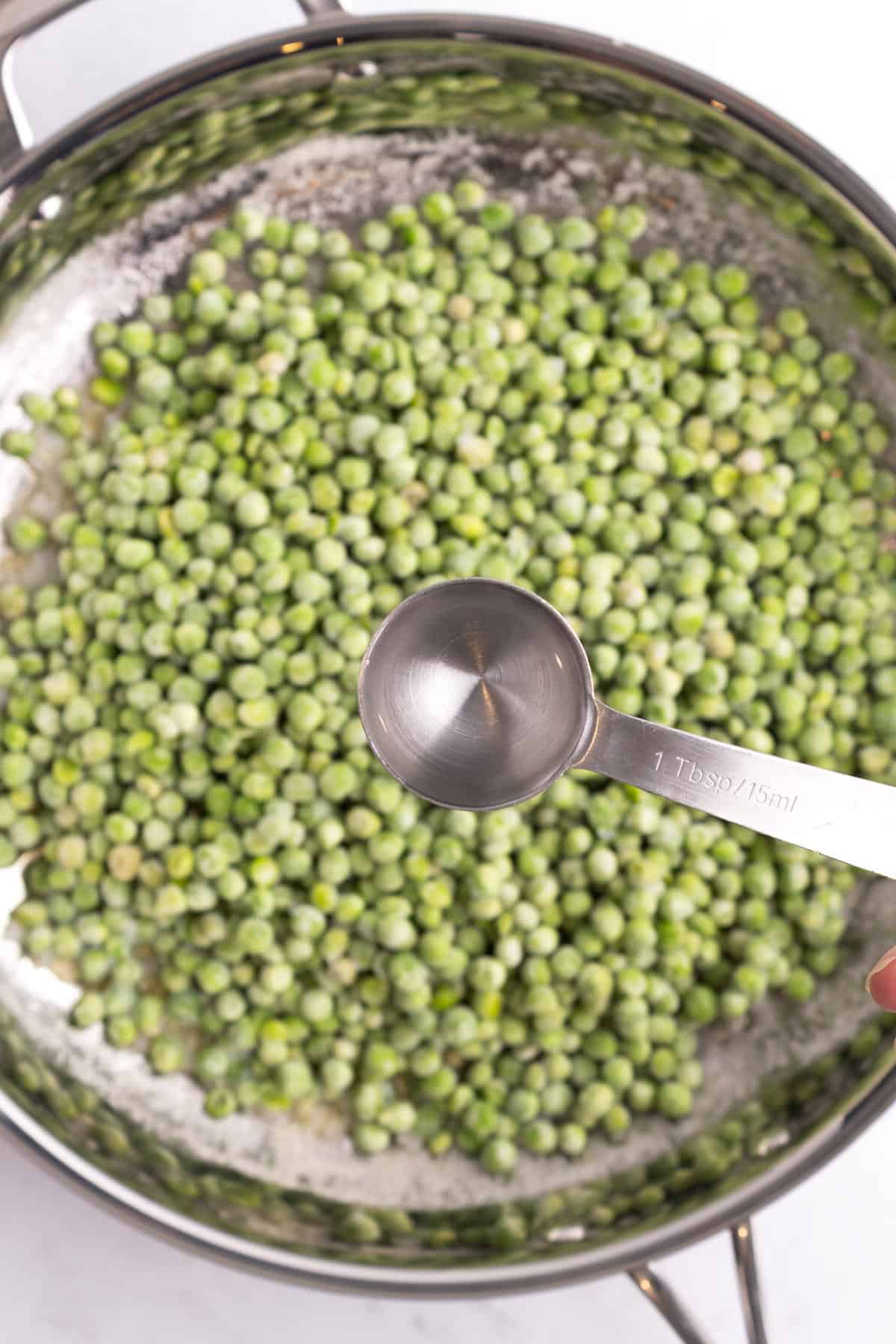 A measuring spoon over a pan of frozen peas.