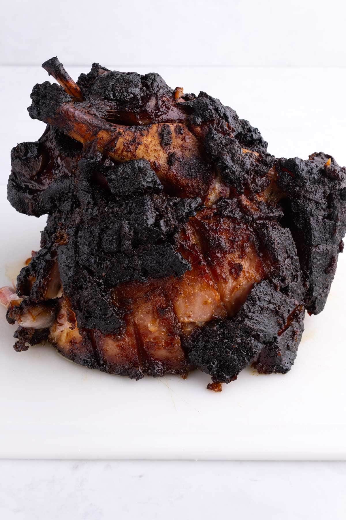 A smoked ham on a white plastic cutting board.