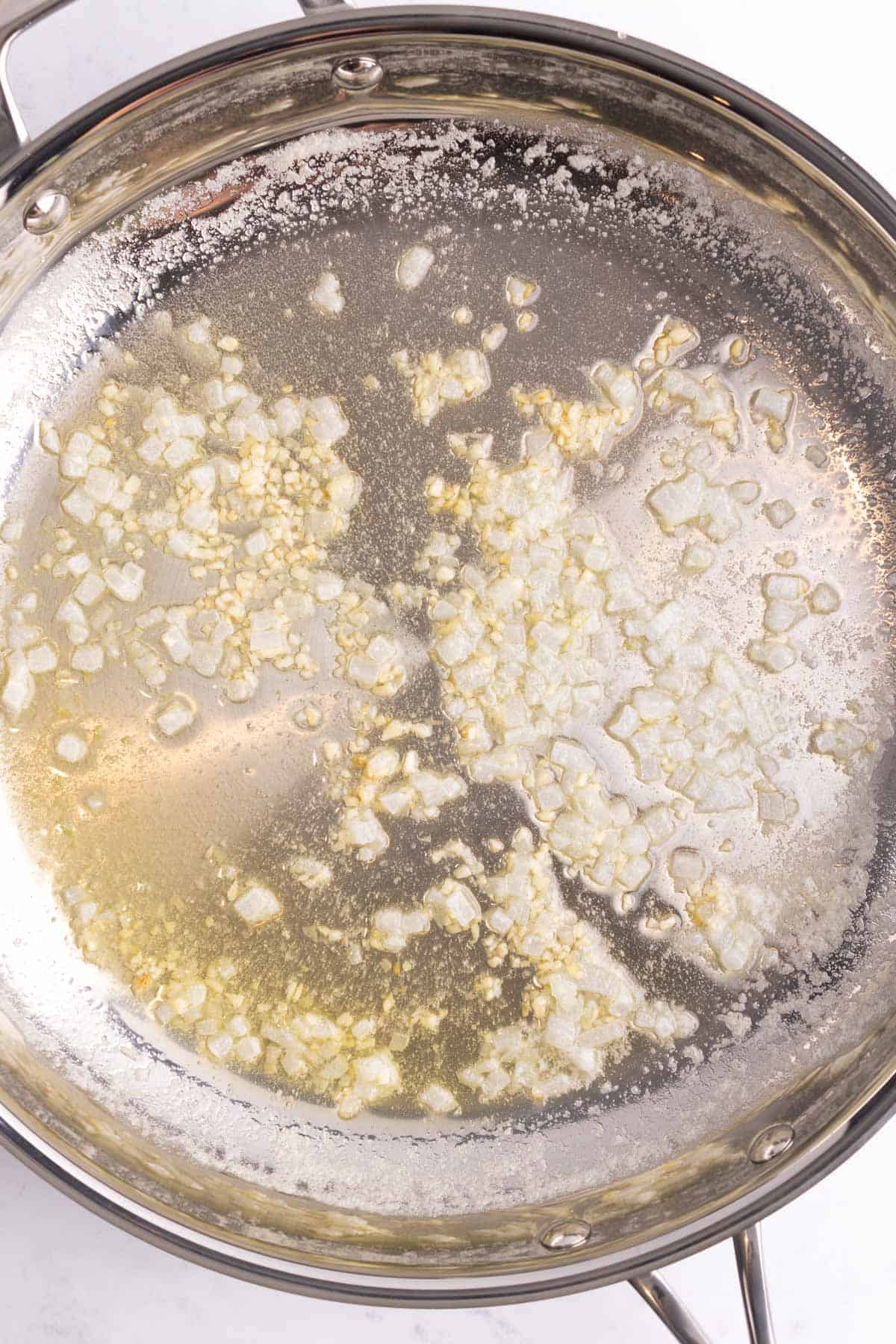 Chopped onions and garlic simmering in a cooking pan.