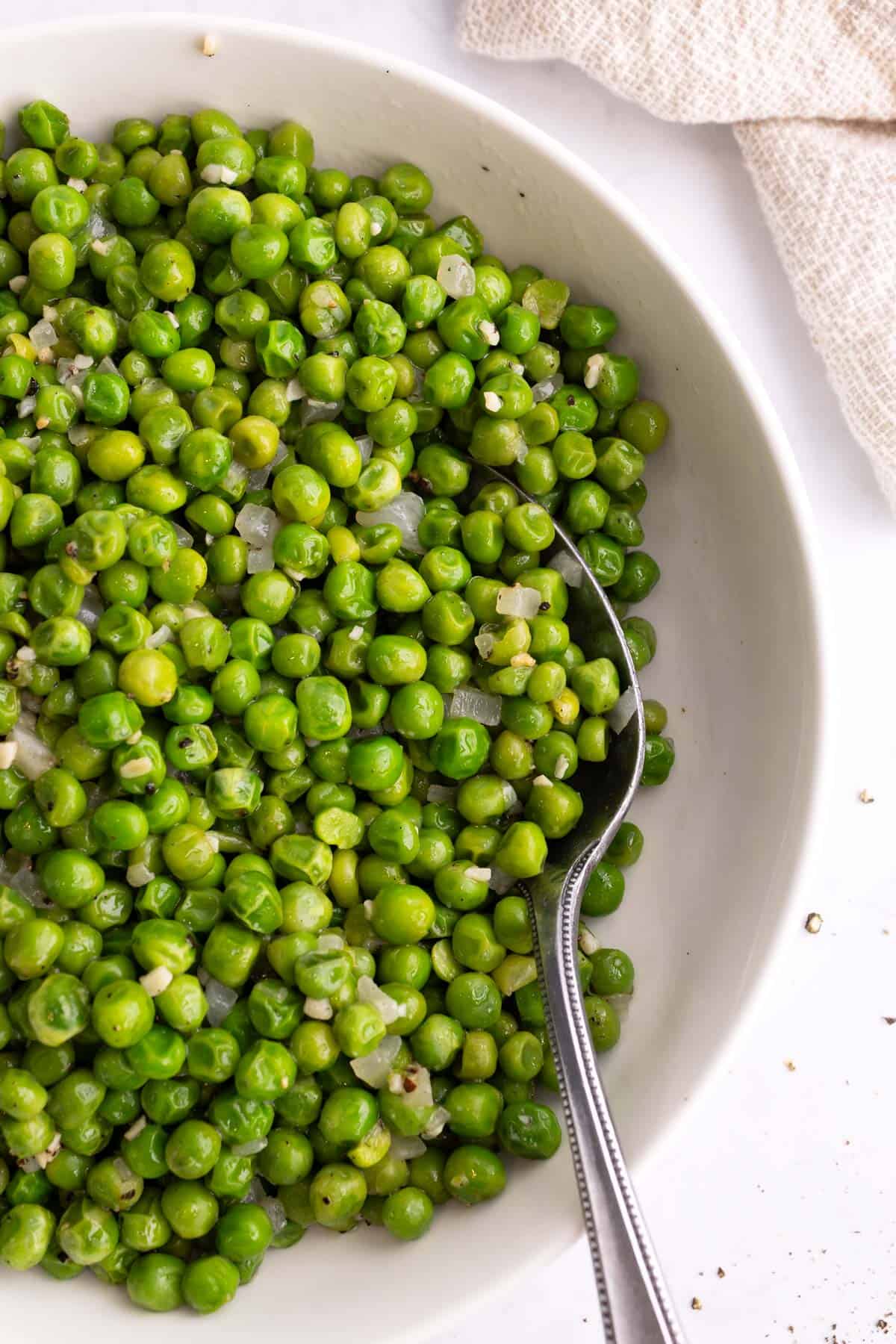 A serving of peas in a white bowl with a spoon.
