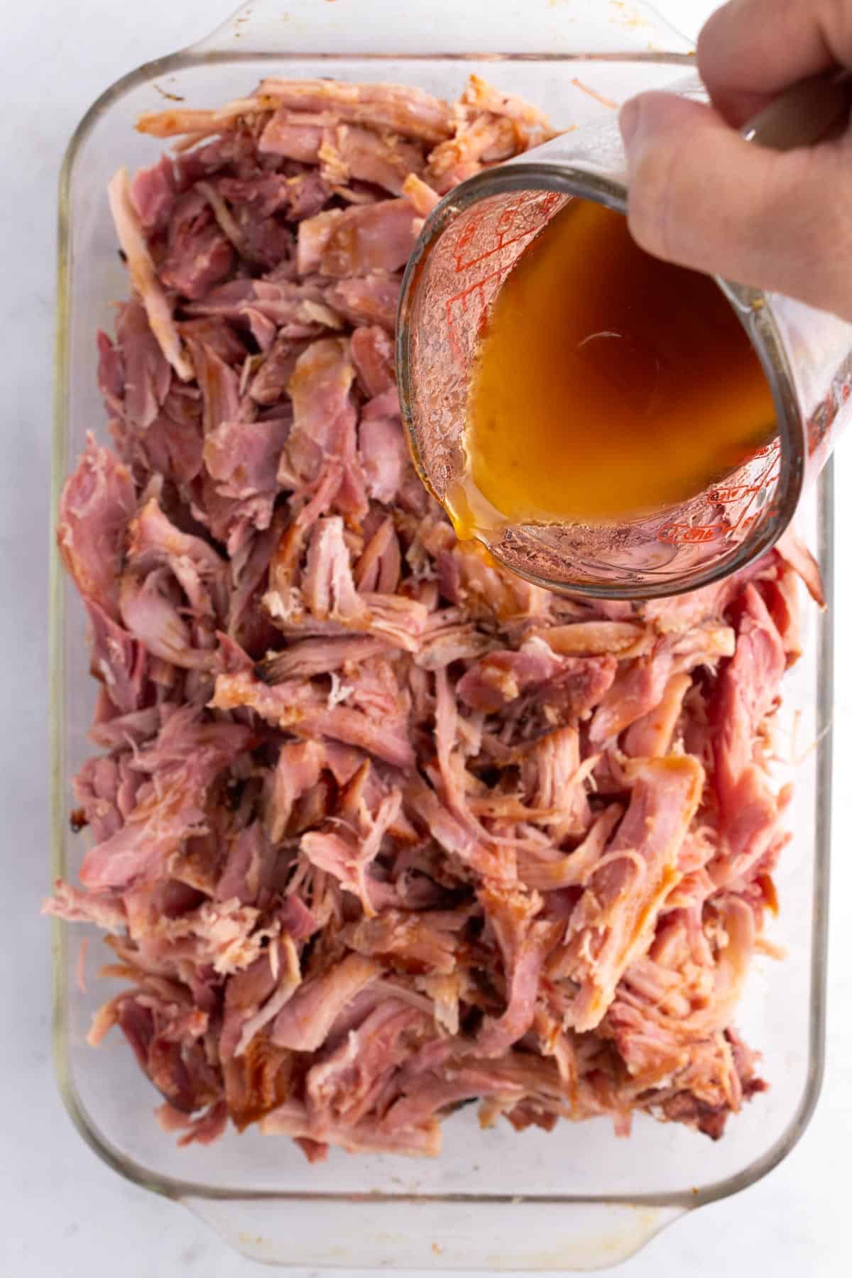 Glaze getting poured onto a pan of shredded ham.