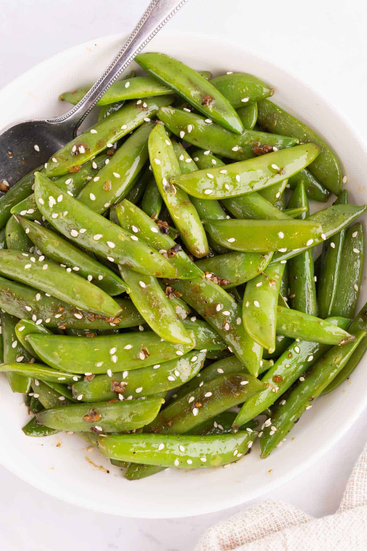 A bowl of sugar snap peas with a spoon.