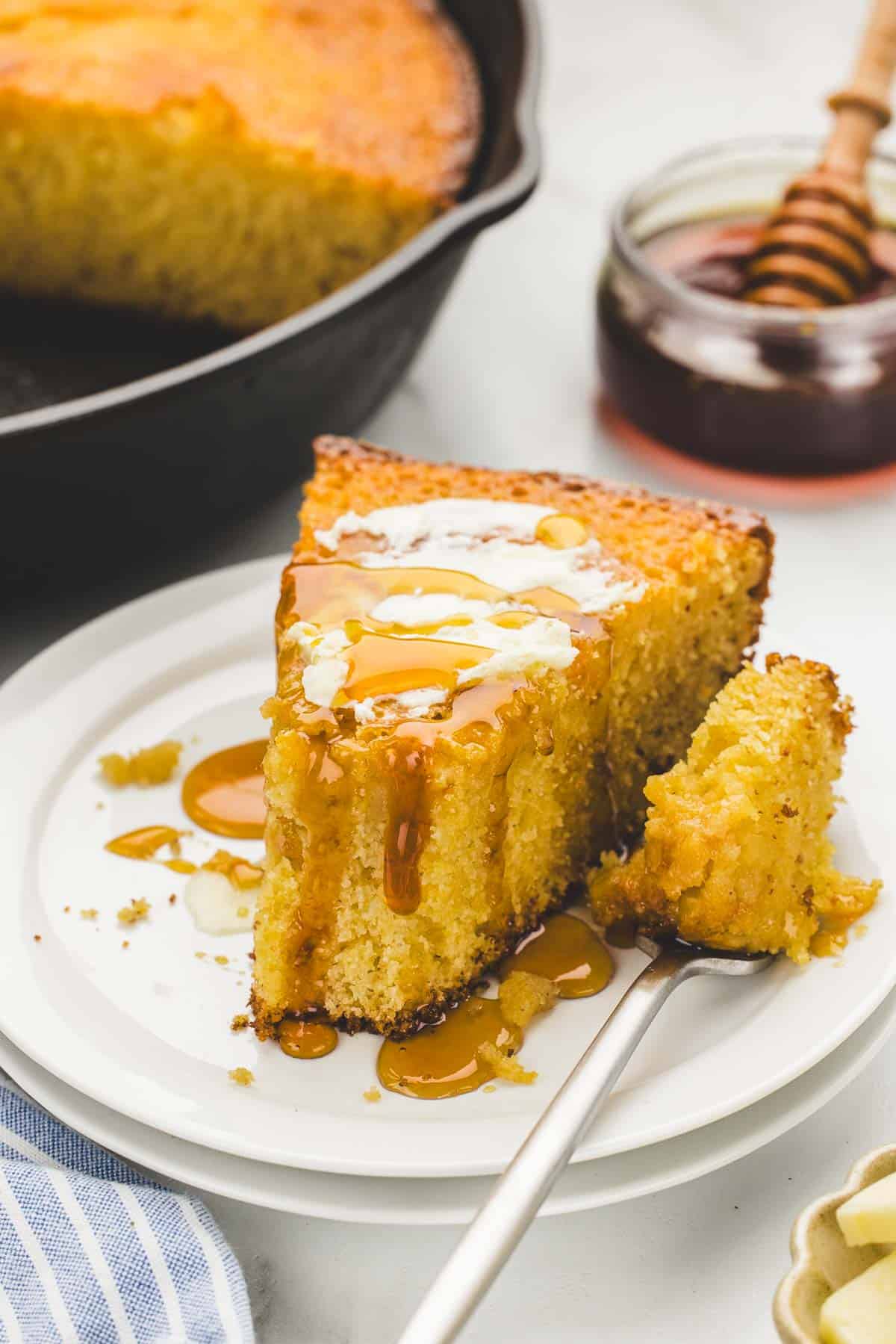 A serving of hot honey cornbread on a small plate with a fork.