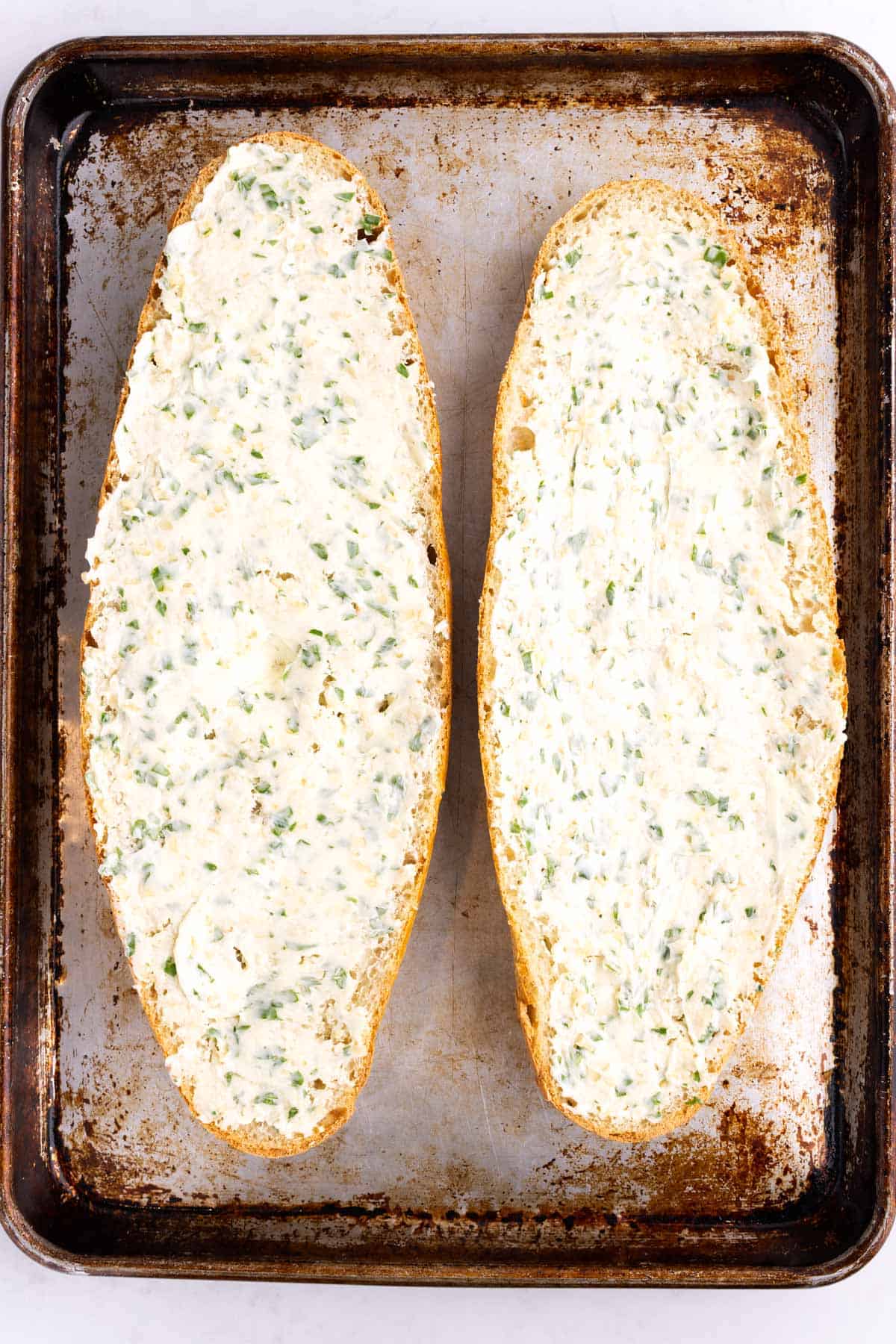 Garlic mixture spread on two pieces of bread on a cookie sheet.
