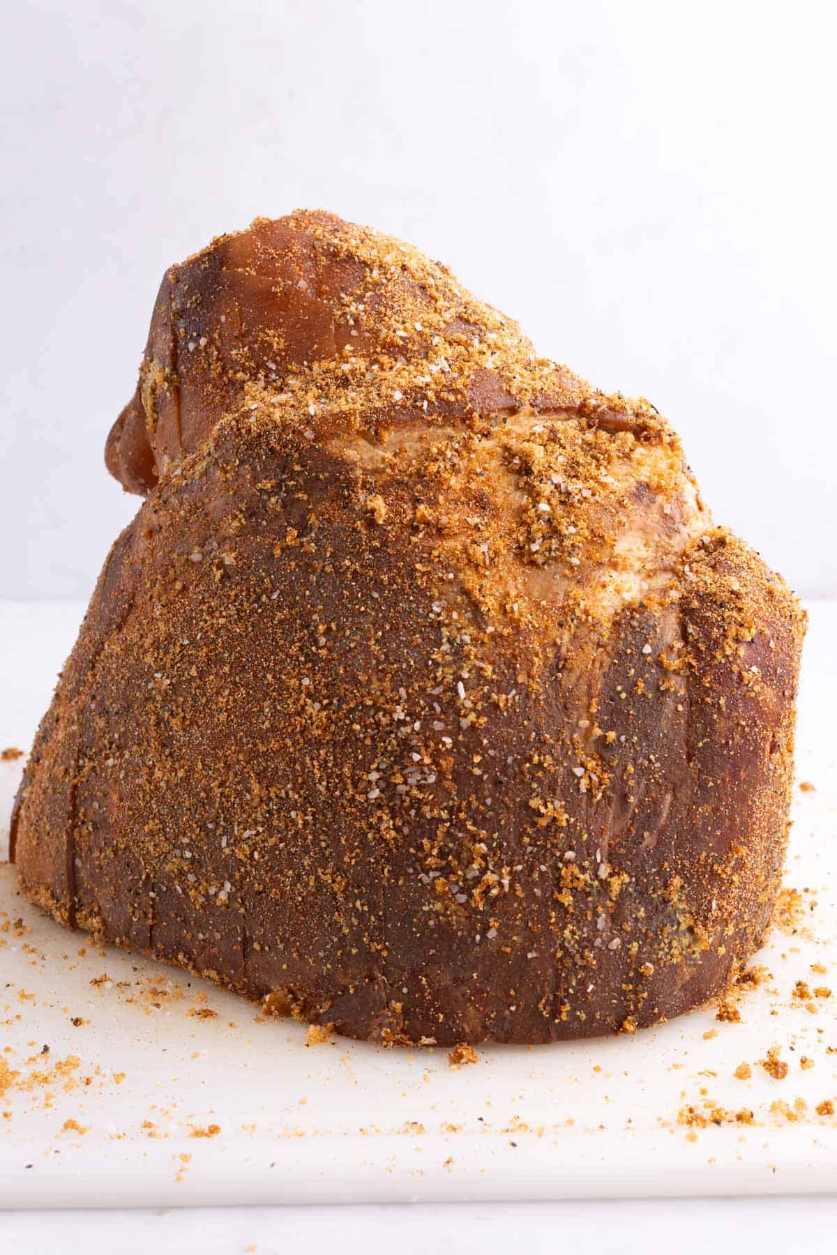 A ham slathered in seasoning on a plastic cutting board.