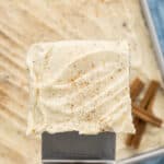 Cream cheese on a square of cake being held by a metal spatula.