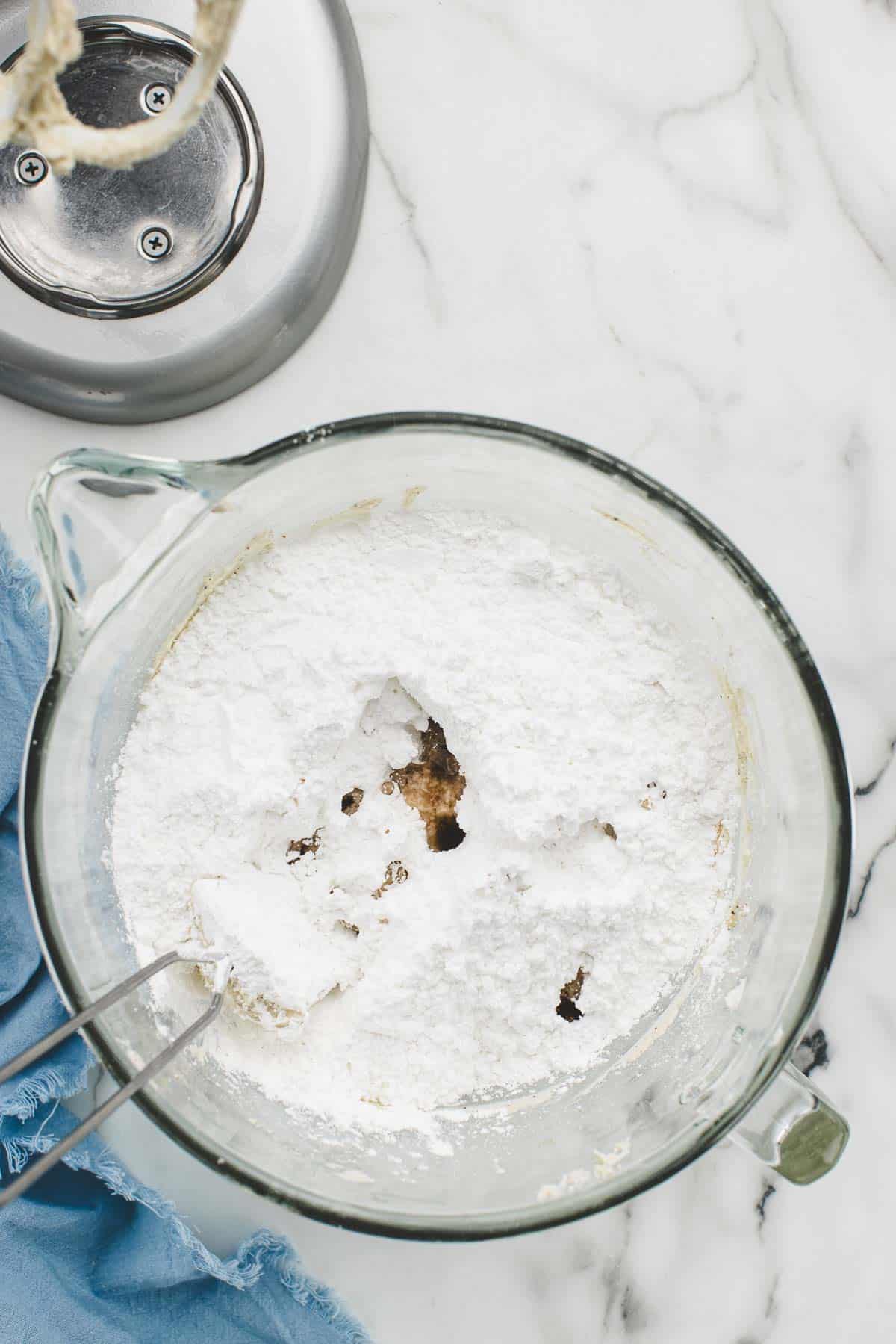 A spatula in a glass bowl of powdered sugar and frosting mix.