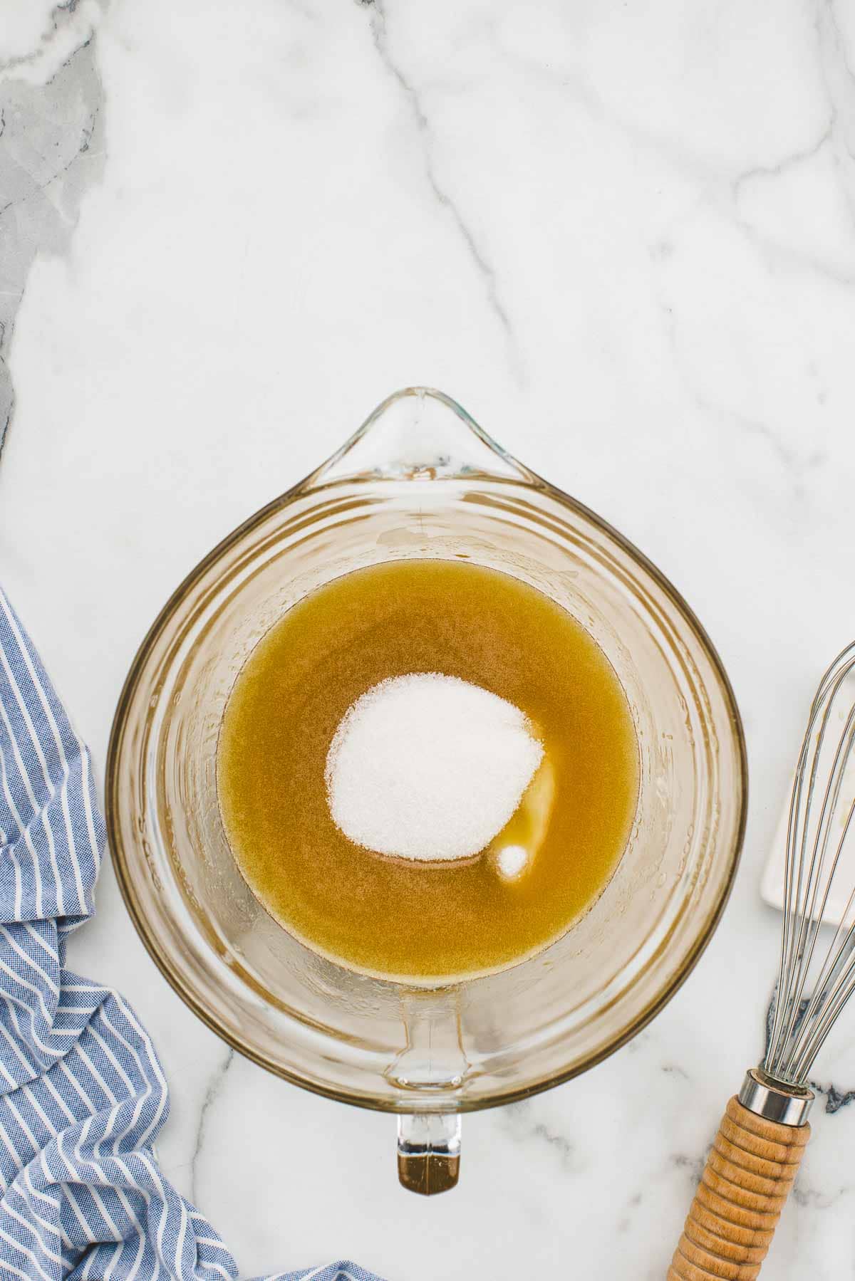 A bowl of unmixed sugar added to hot honey with a whisk beside it.