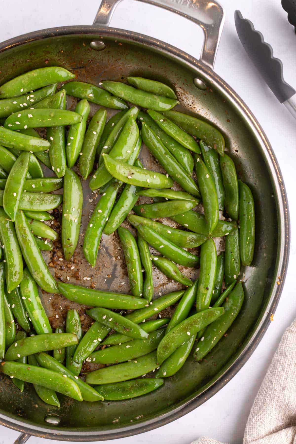A pan full of sauteed snap peas topped with seeds.