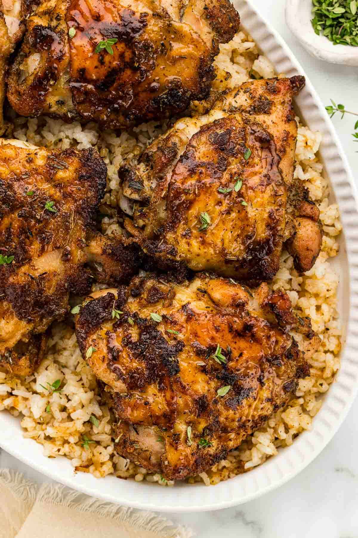 A white serving platter of chicken thighs on rice.