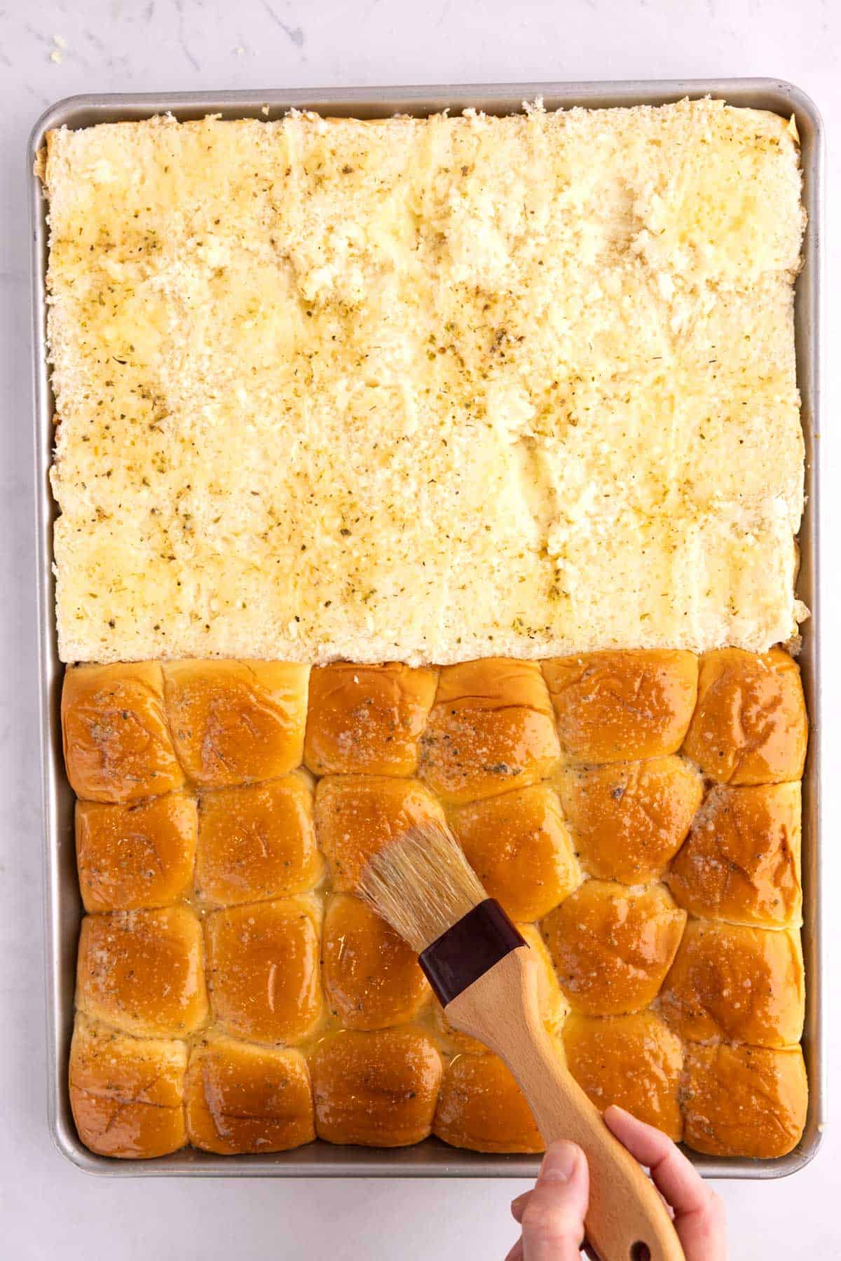 A tray of slider bread with a cooking brush coating it.